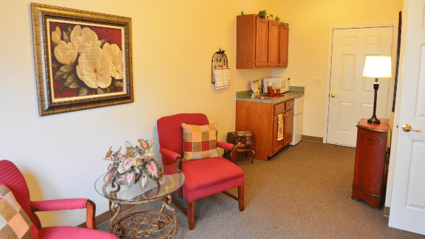 A cozy living space with red chairs, a small table, and a kitchenette.