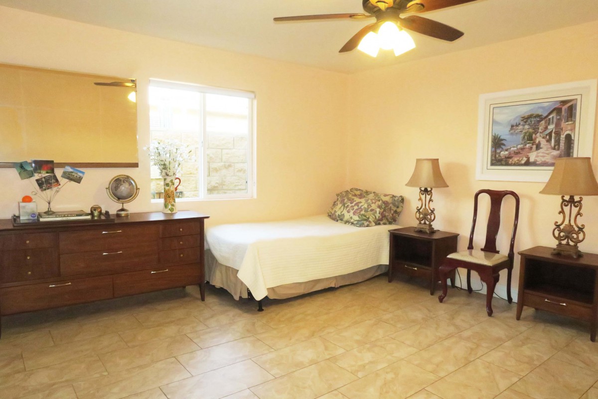 A cozy bedroom featuring a single bed, a dresser with a mirror, a lamp on a side table, and a comfortable chair.