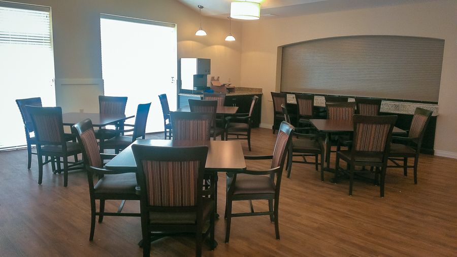 An empty dining area with wooden tables and chairs, featuring a bar section in the background.