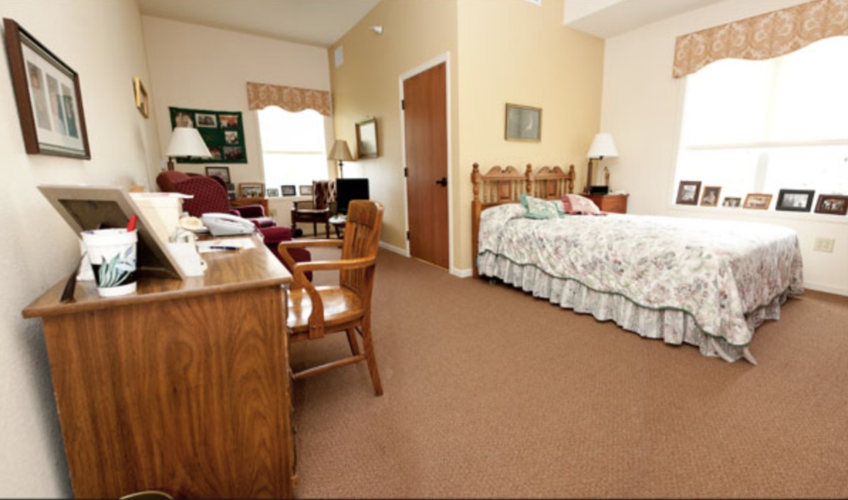 A cozy bedroom with a wooden bed, desk, and chair, featuring warm lighting and homey decor.