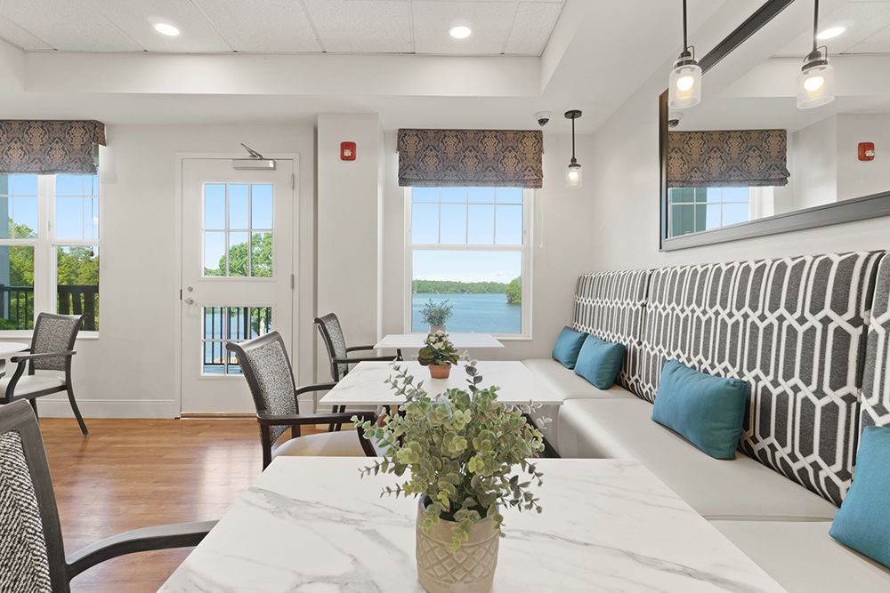 A cozy and bright dining area with a view of the outdoors, featuring tables, chairs, and decorative plants.