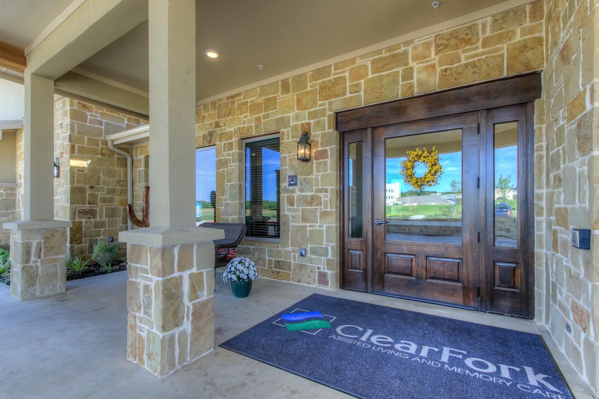 A welcoming entrance with a stone facade and decorative wreath, featuring a glass door and an outdoor seating area.