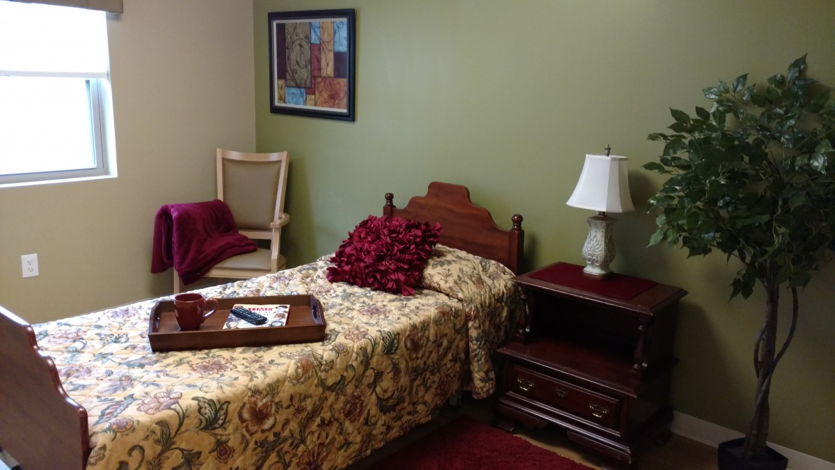 A cozy bedroom with a single bed, nightstand with a lamp, and a painting on the wall.