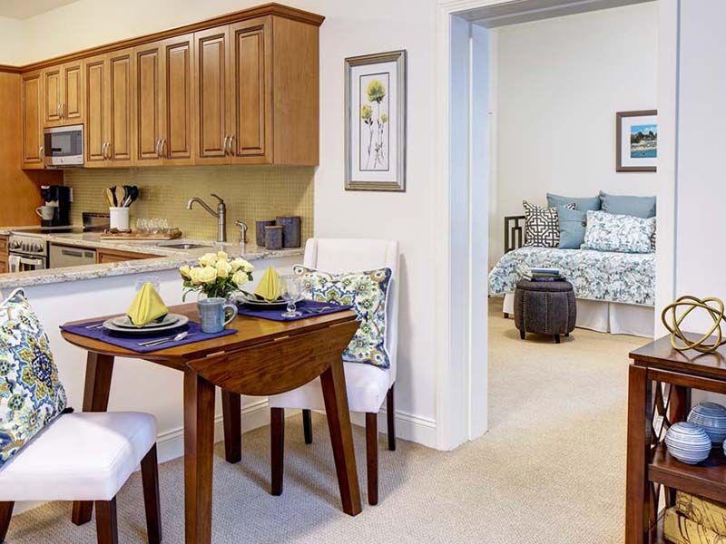 A cozy apartment interior featuring a small dining area with a kitchen and a glimpse into the bedroom.