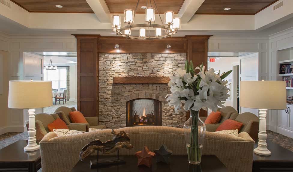 A cozy living room with a brick fireplace, elegant chandelier, and floral decoration.