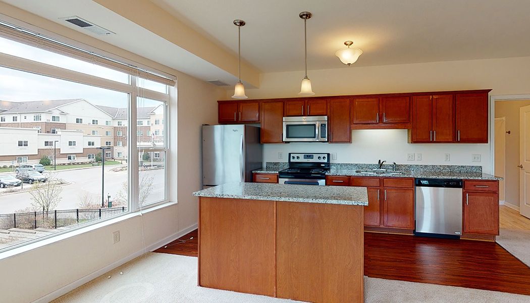 A modern kitchen featuring stainless steel appliances, wooden cabinetry, and a central countertop island with pendant lighting.