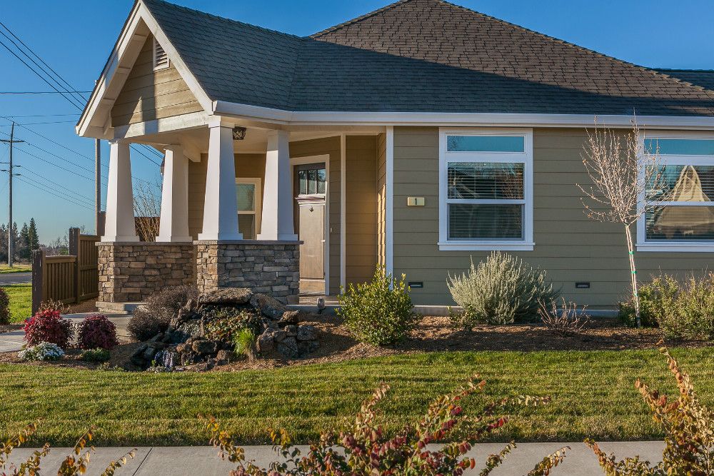 A single-story house with a porch and landscaped front yard on a sunny day.