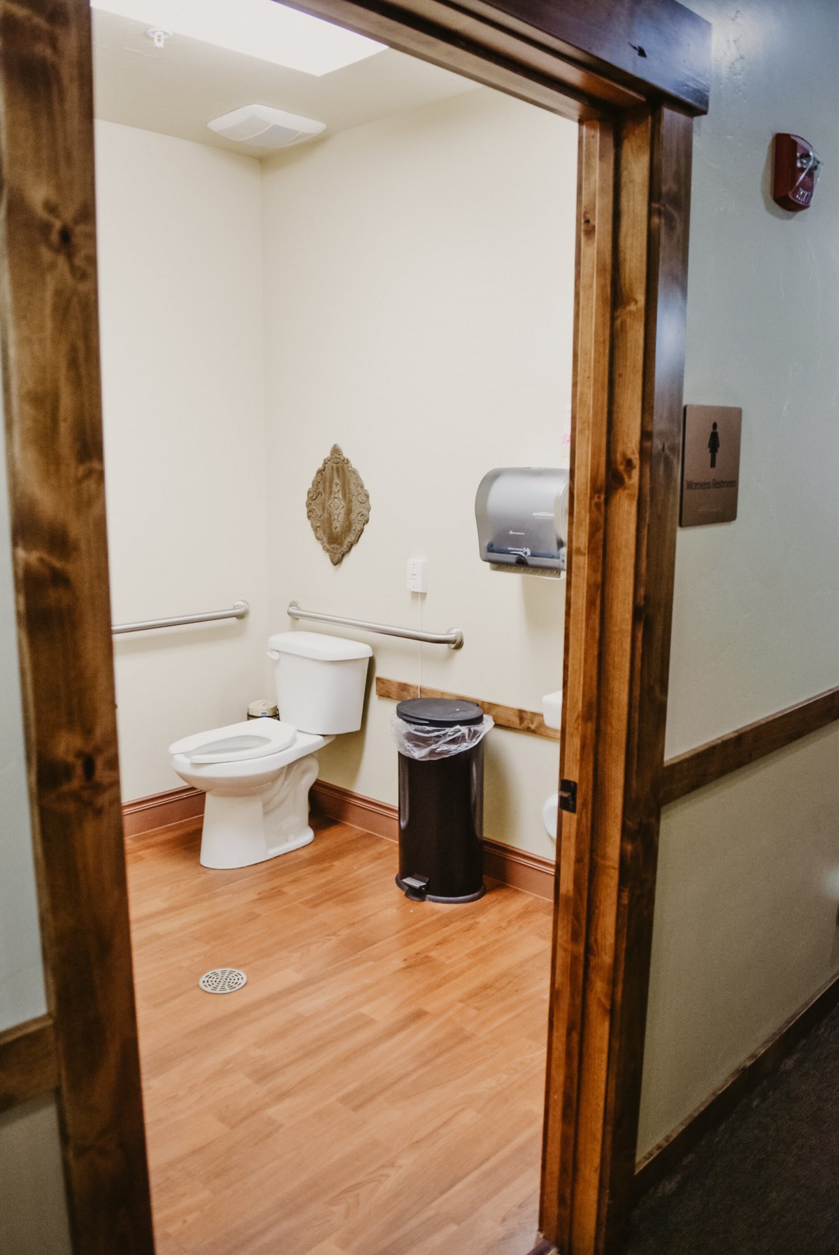 A clean and accessible bathroom with a toilet, trash can, and handrails.
