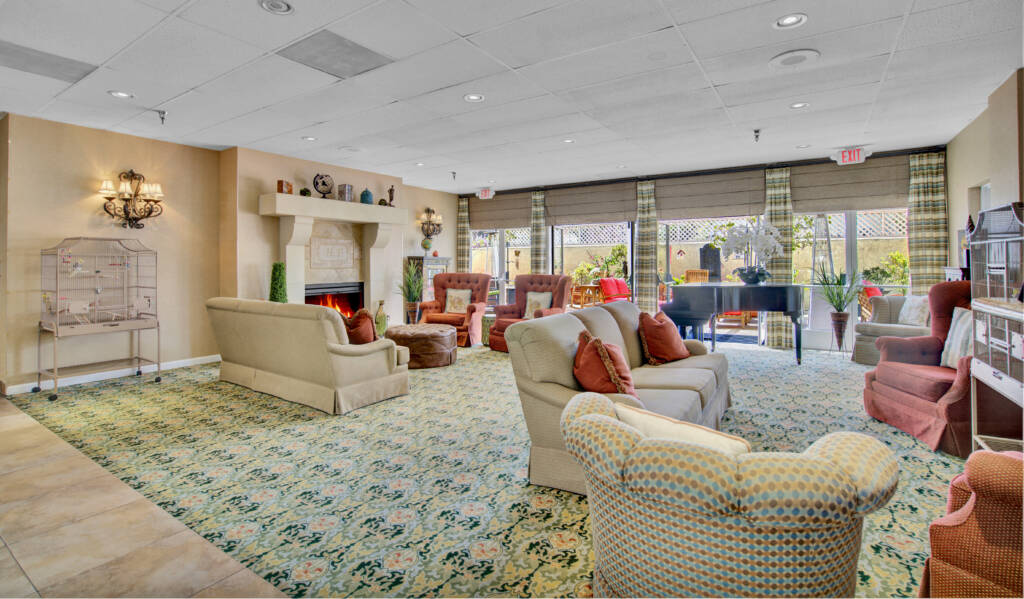A spacious lounge with comfortable sofas, a fireplace, and a grand piano by large windows.