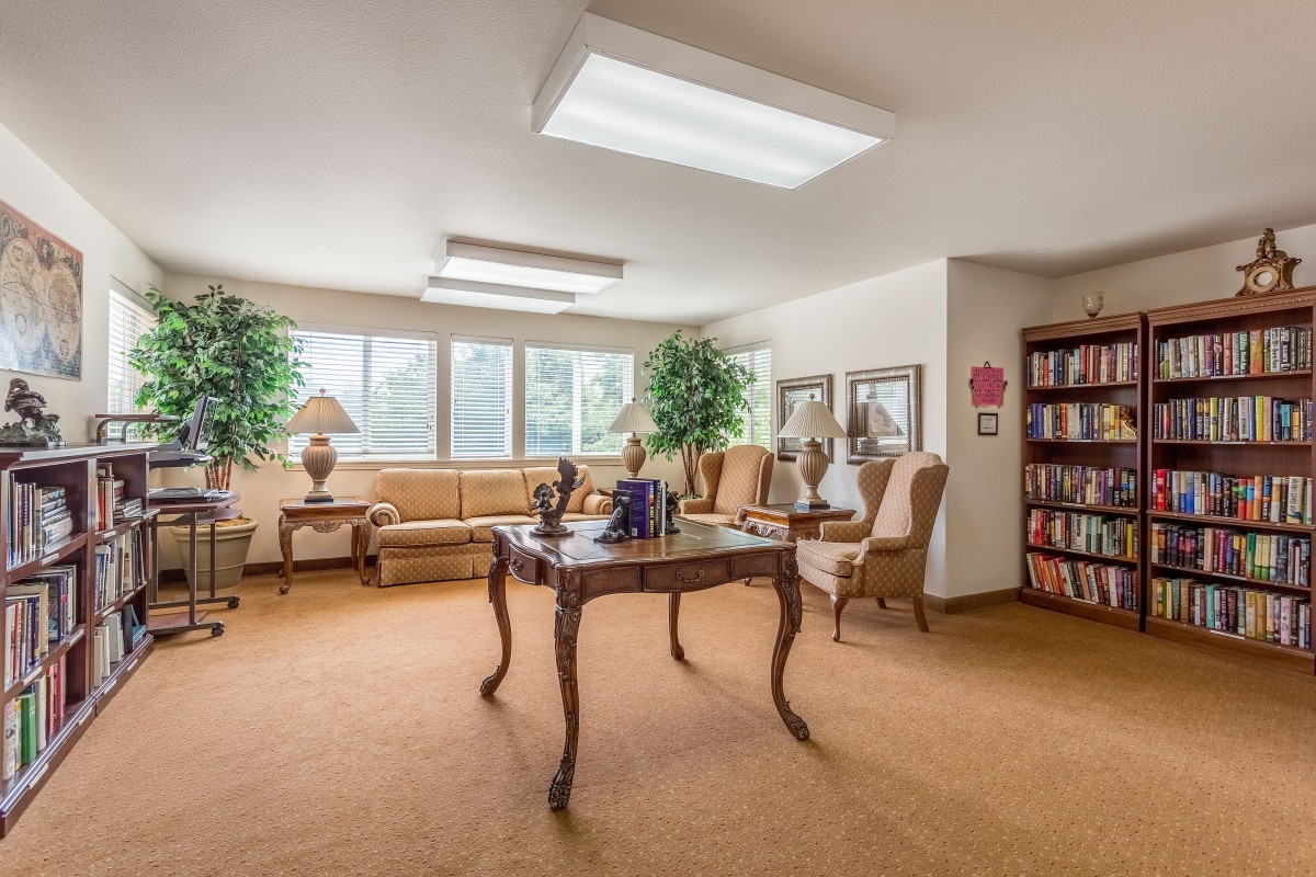 A cozy and elegantly furnished living room with a large window, featuring a sofa, chairs, bookshelf, and decorative plants.