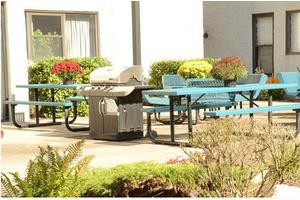 An outdoor patio area with a barbecue grill, tables, and benches surrounded by colorful flowers.