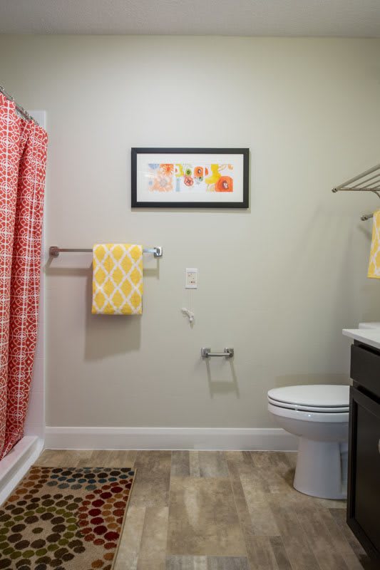 A well-organized bathroom featuring a red shower curtain, yellow towels, and a framed artwork on the wall.
