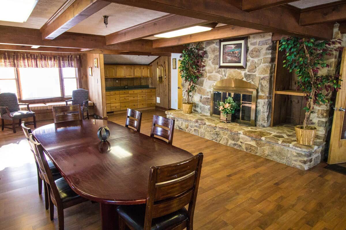 A cozy rustic dining room with a wooden table, chairs, and a stone fireplace.