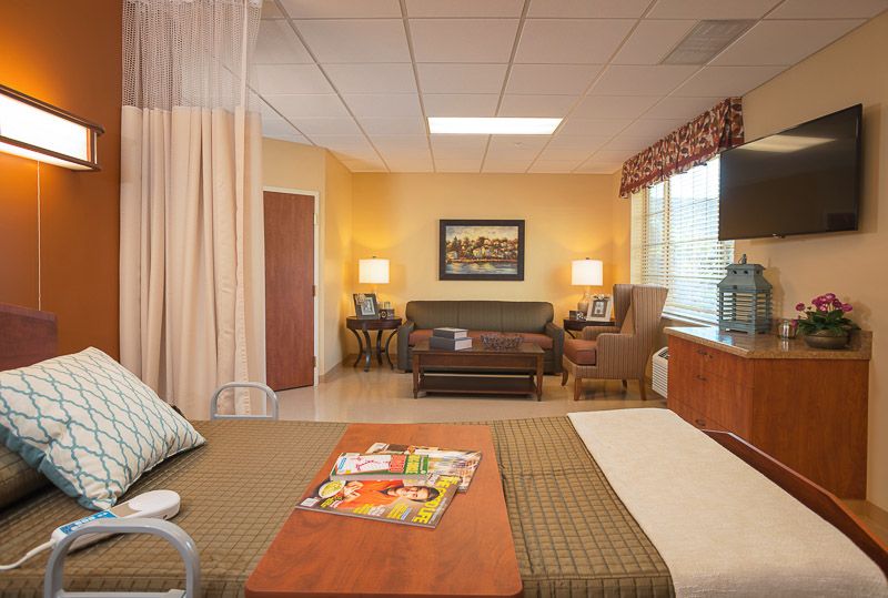 A well-furnished hospital room featuring a bed, sofa, and a window with natural light.