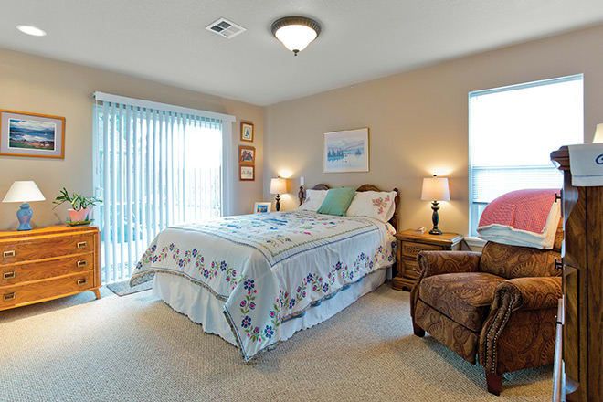 A cozy bedroom with a neatly made bed, two bedside lamps, and a comfortable chair by the window.