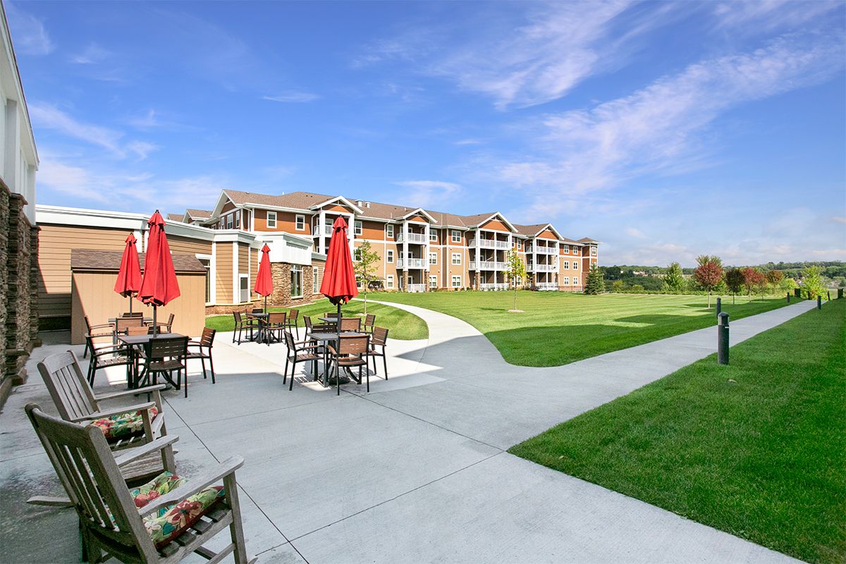 A modern apartment complex with outdoor seating and red umbrellas on a sunny day.