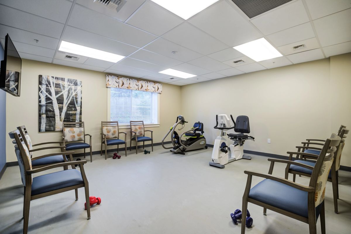 A well-lit exercise room with fitness equipment and seating, designed for physical therapy activities.