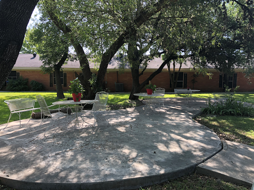 A serene outdoor space featuring shaded seating under large trees.