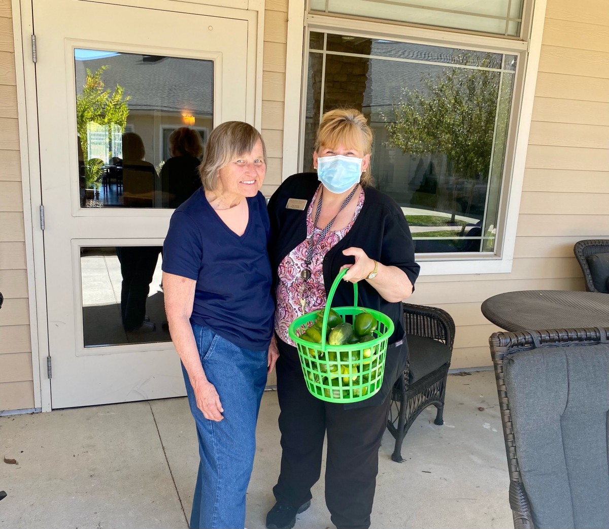 Two individuals standing outside a building, one holding a green basket.