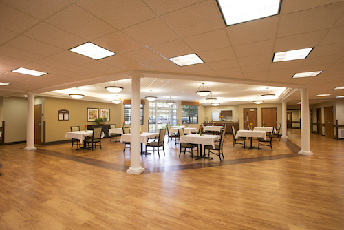 A spacious and thoughtfully designed dining area with tables set for guests, featuring warm lighting and wooden flooring.