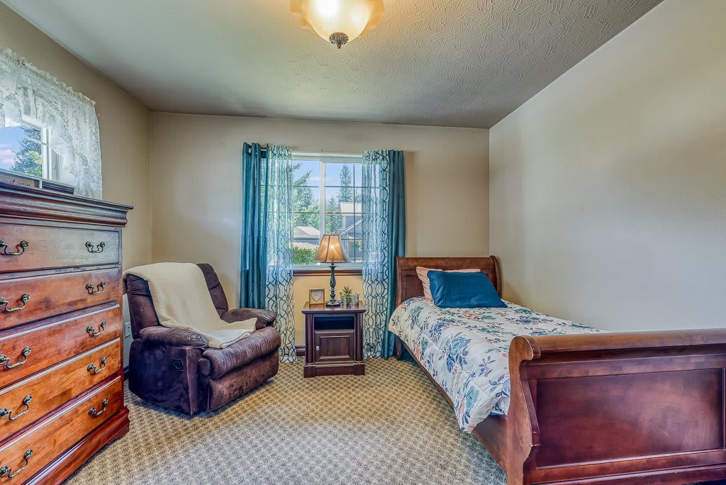 A cozy bedroom with a single bed and armchair by the window.