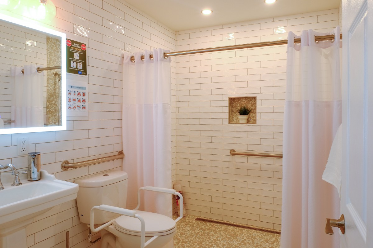 A modern, accessible bathroom featuring a walk-in shower with grab bars and white tile walls.