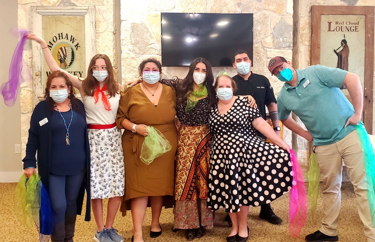 A group of people wearing masks and colorful outfits, posing together indoors.