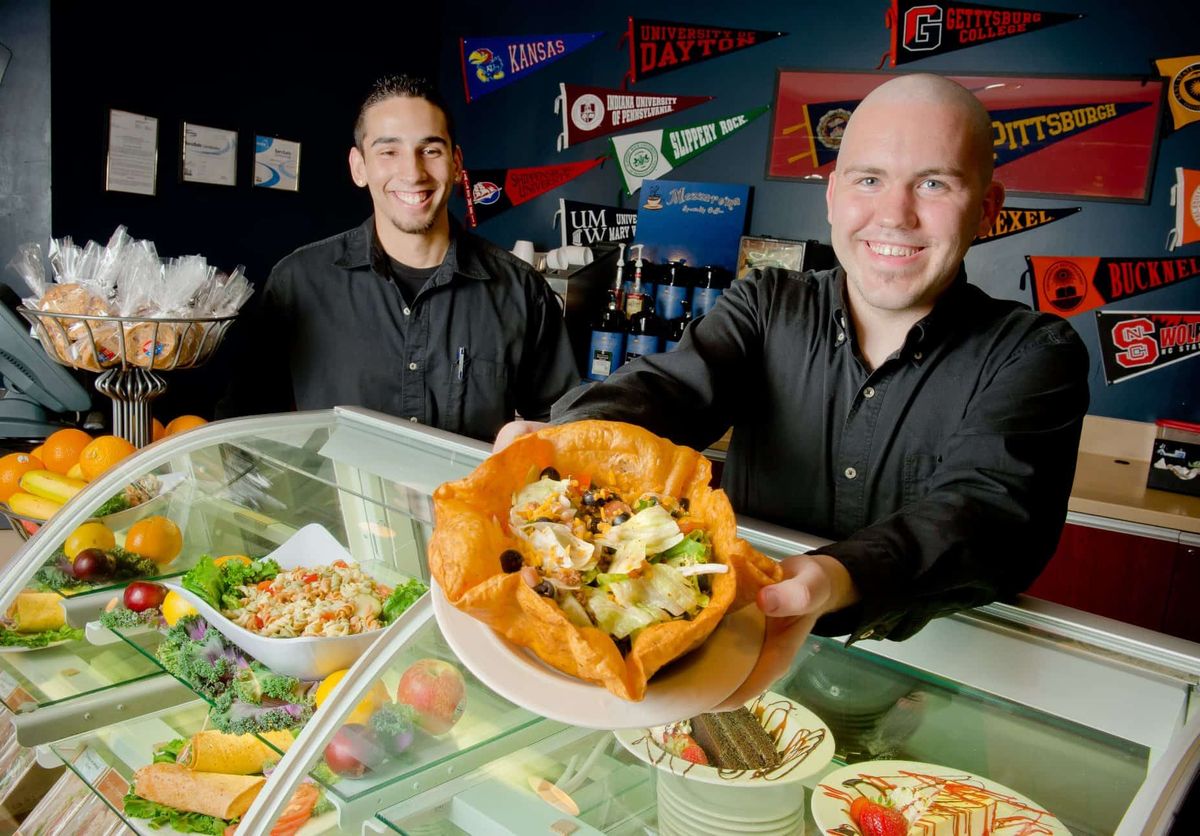 Two staff members at a restaurant presenting a taco salad at the counter.