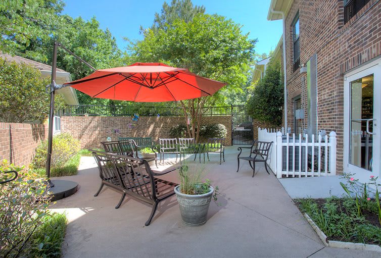 A cozy patio with outdoor seating and a large red umbrella, surrounded by greenery.