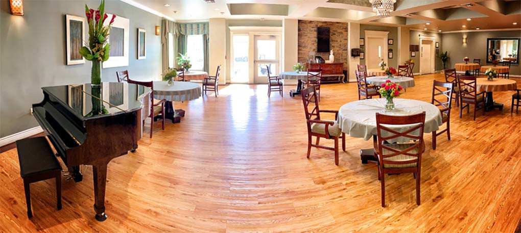 A bright and spacious dining room with wooden floors, featuring round tables and chairs.