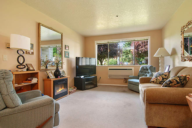 A cozy living room with a sofa, armchair, and a large window overlooking a garden.
