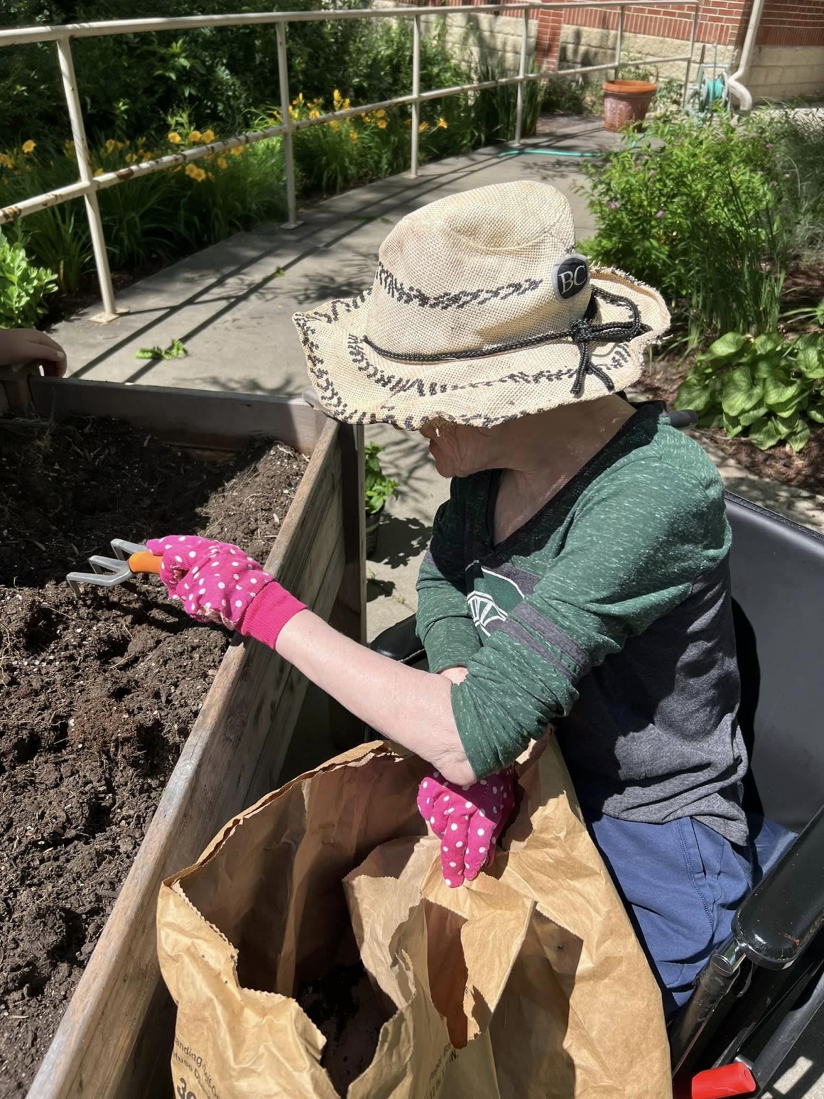 A person gardening outdoors, wearing a hat and gloves while working with soil.