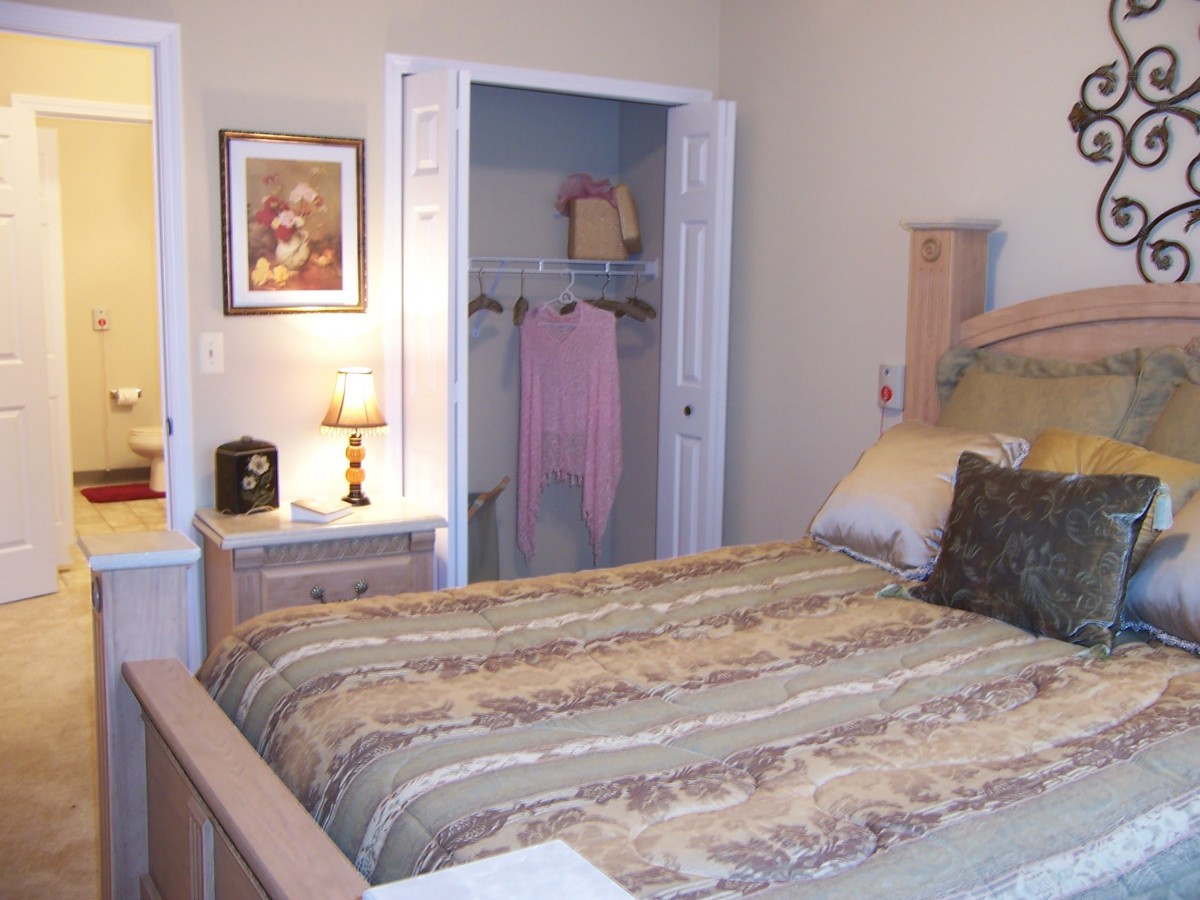 A cozy bedroom with a neatly made bed, an open closet, and a small lamp on the nightstand.