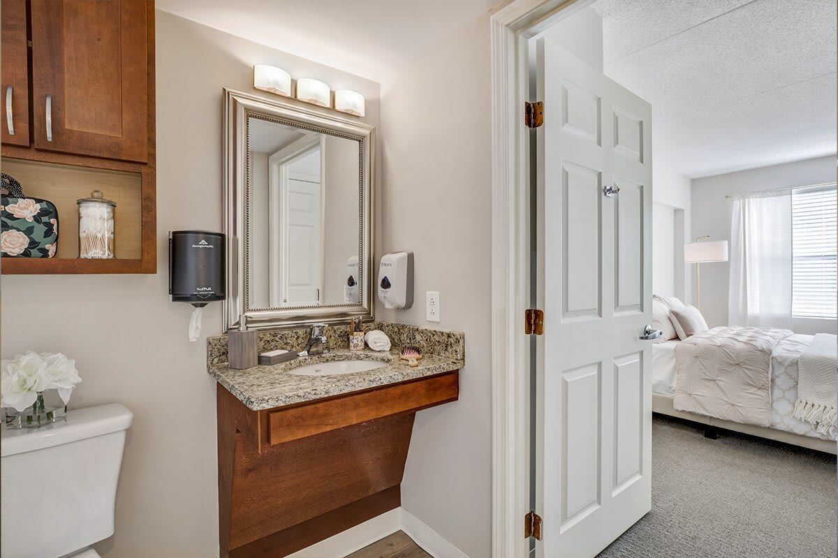 A modern bathroom with a granite-topped vanity and well-lit mirror.
