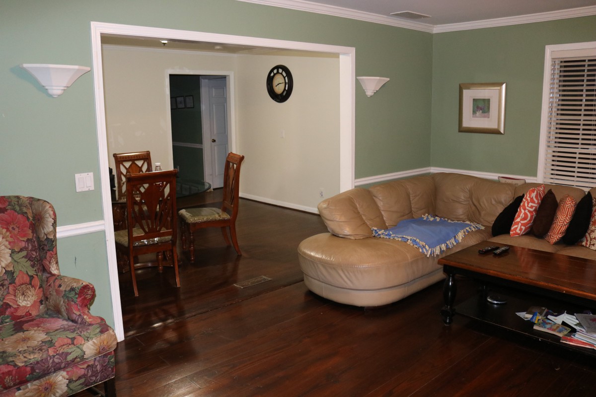 A cozy living room featuring a leather sofa and adjoining dining area with wooden chairs, set against green walls and wood flooring.