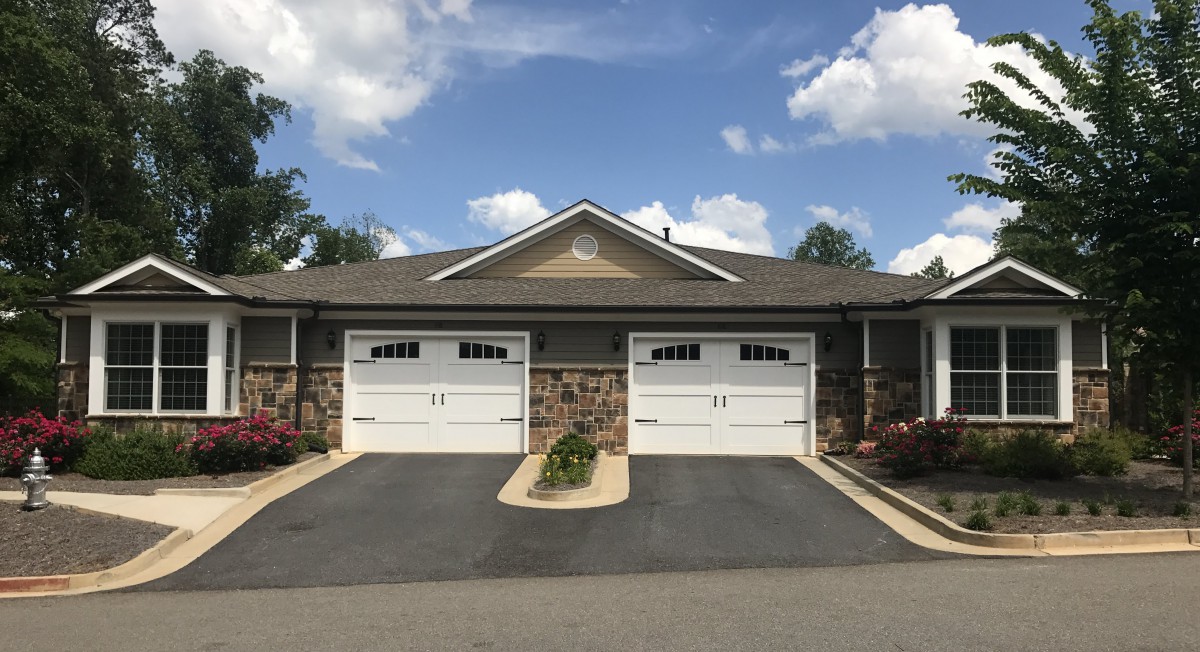 A duplex with two garage doors and a shared driveway under a partly cloudy sky.