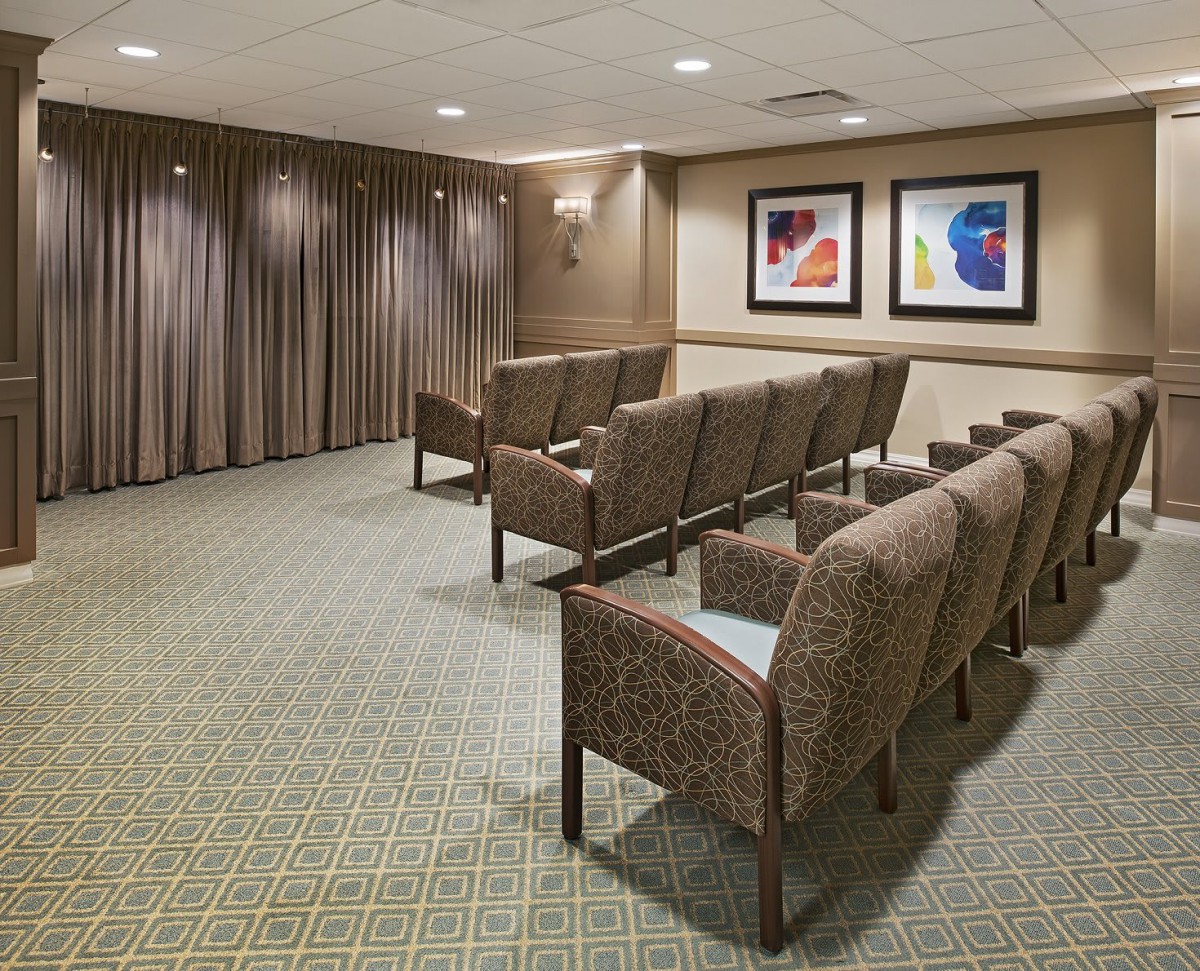 A small seating area with rows of upholstered chairs, carpeted floor, and framed artwork on the wall.