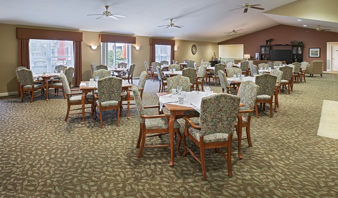 A spacious dining area with multiple set tables and chairs, ceiling fans, and a carpeted floor.
