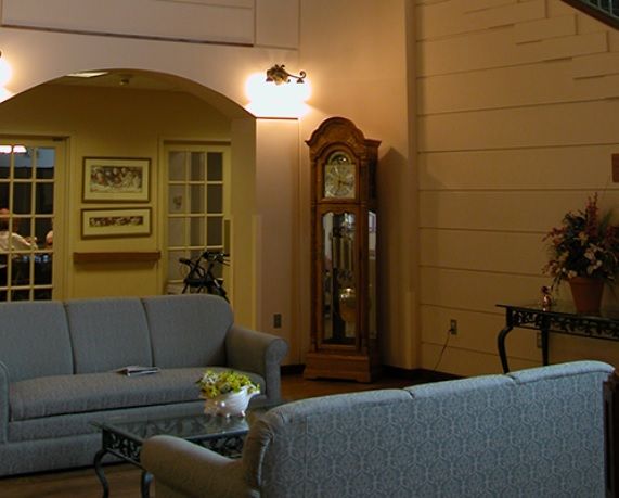 A cozy living room featuring a sofa set, a grandfather clock, and wall art.