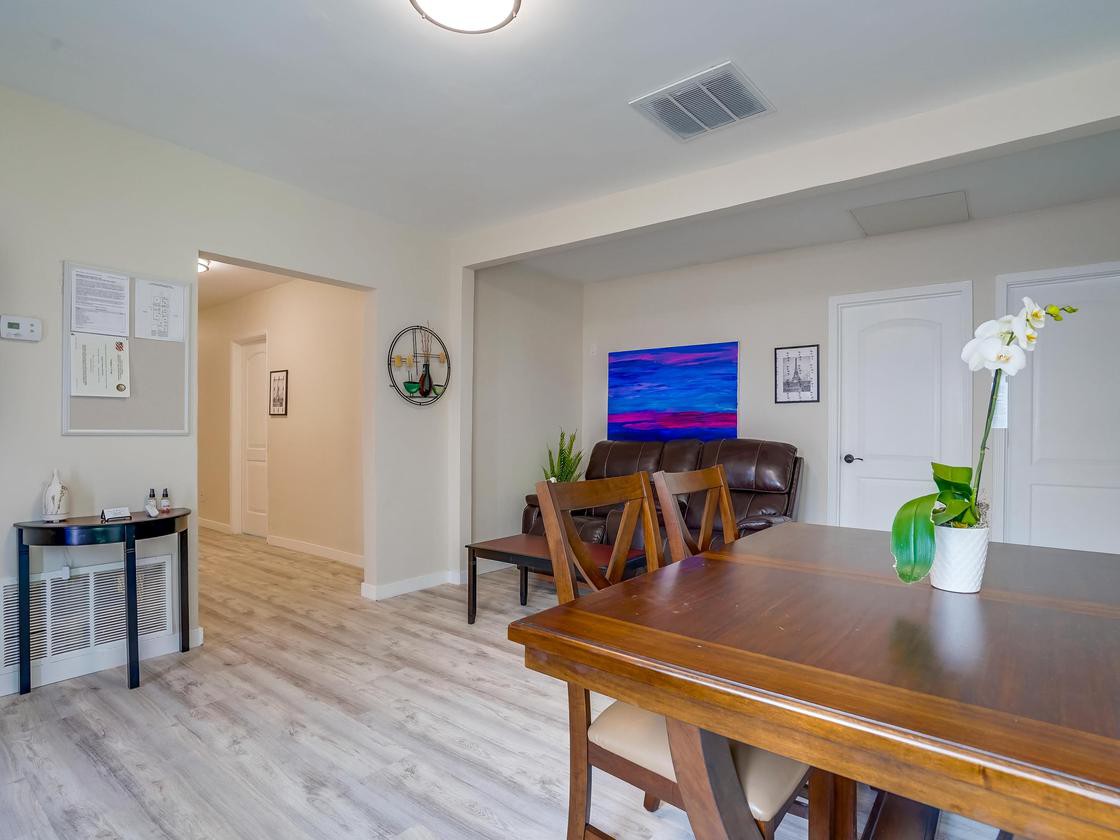 A modern living space featuring a dining table, television, and indoor plants with wood flooring.