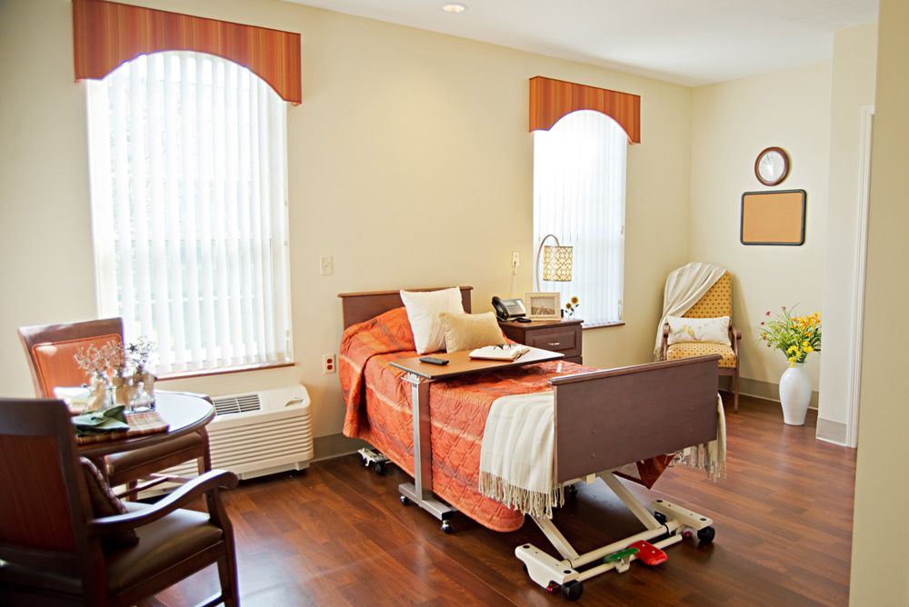 A comfortable and well-lit hospital room featuring a bed, seating area, and large windows.