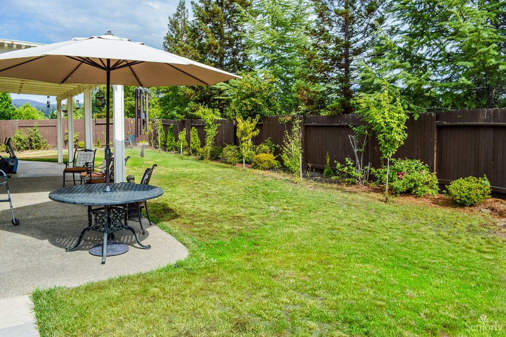 A serene backyard with a patio set under an umbrella, surrounded by a lush green lawn and trees.