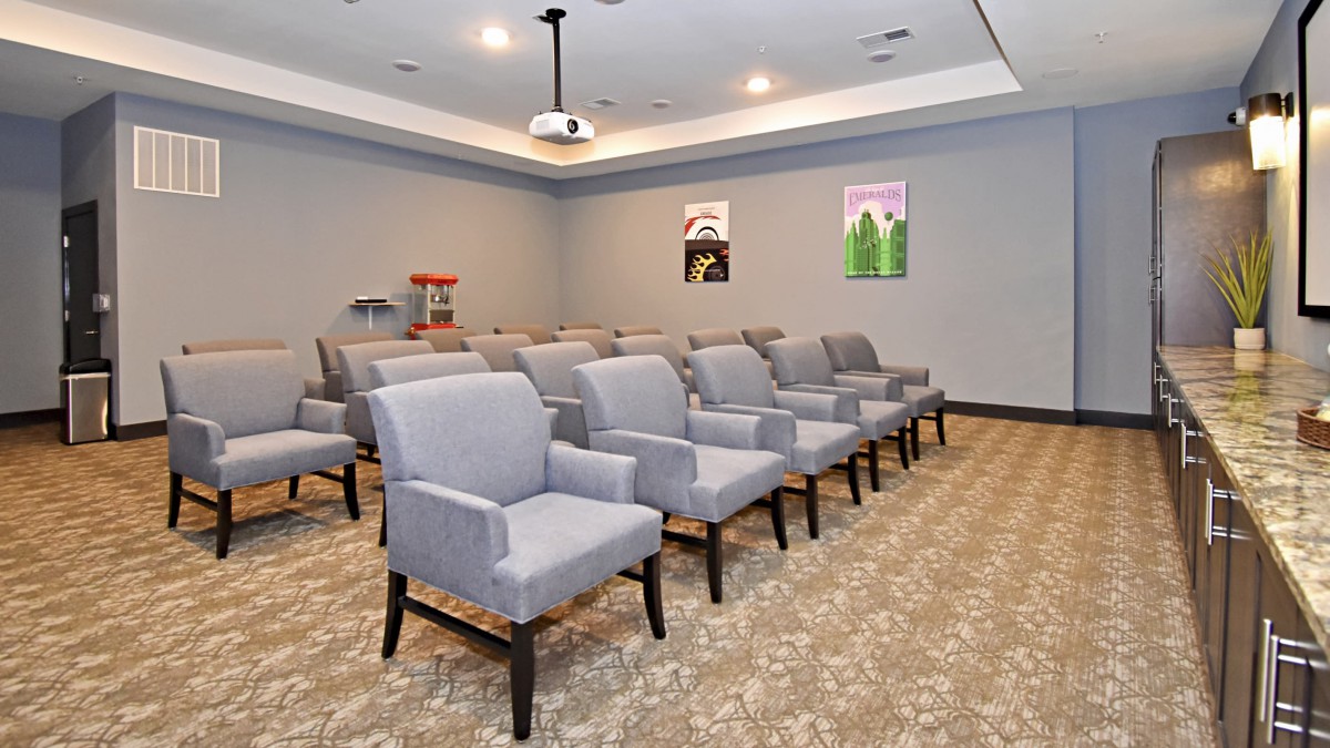 A cozy home theater with rows of plush chairs and a ceiling-mounted projector.