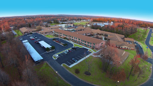 Aerial view of a hotel surrounded by autumn foliage and a spacious parking lot.