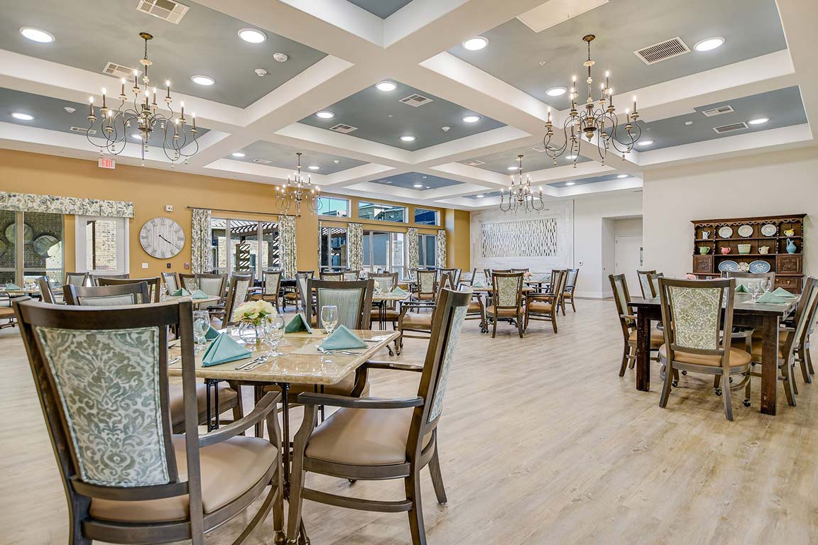 An elegant dining area with neatly arranged tables and chairs, illuminated by stylish chandeliers.