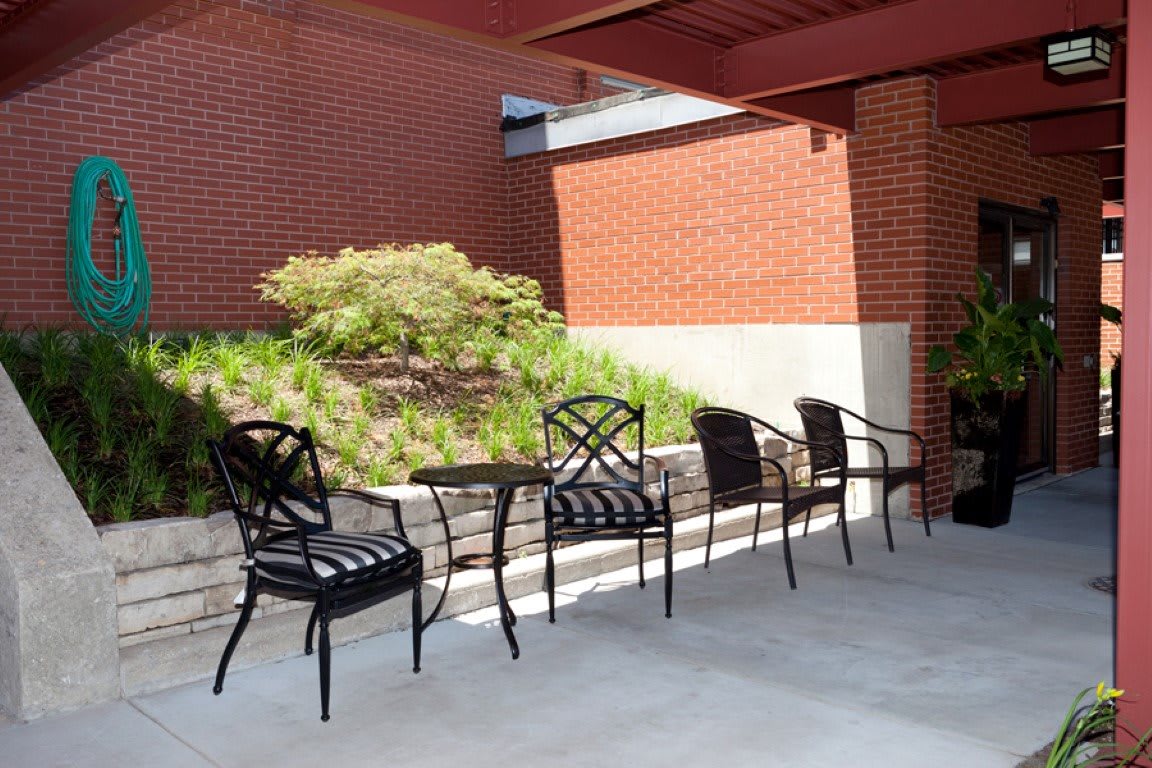 A shaded patio area with chairs and a table against a brick wall.