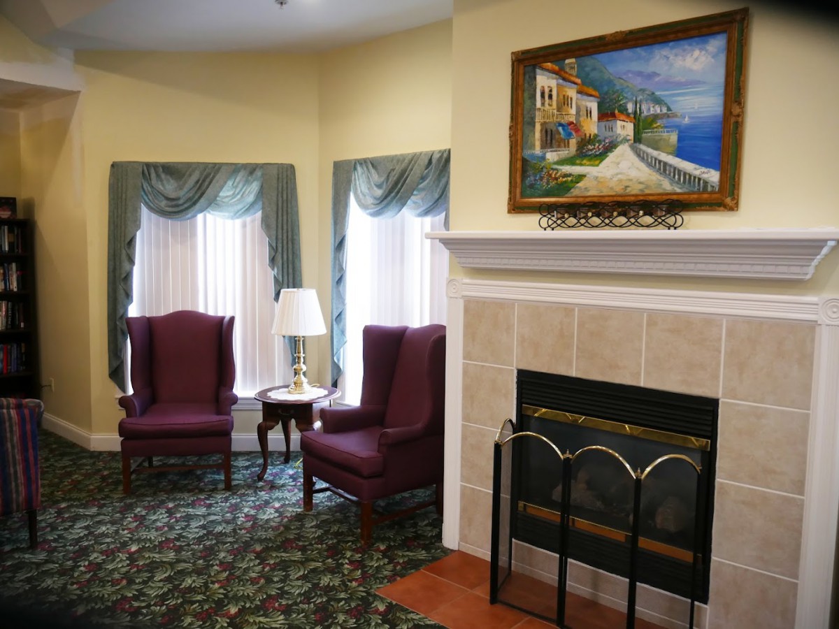 A cozy living room featuring a fireplace, two armchairs, and a colorful painting above the mantel.