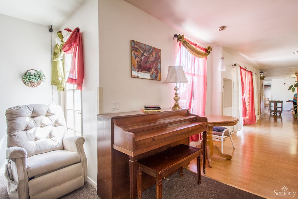 A cozy living room featuring a piano, armchair, and decorative curtains.