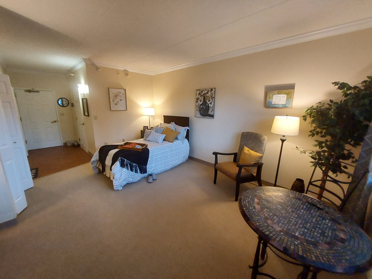 A cozy and well-decorated bedroom with a bed, chairs, lamps, and artwork on the walls.