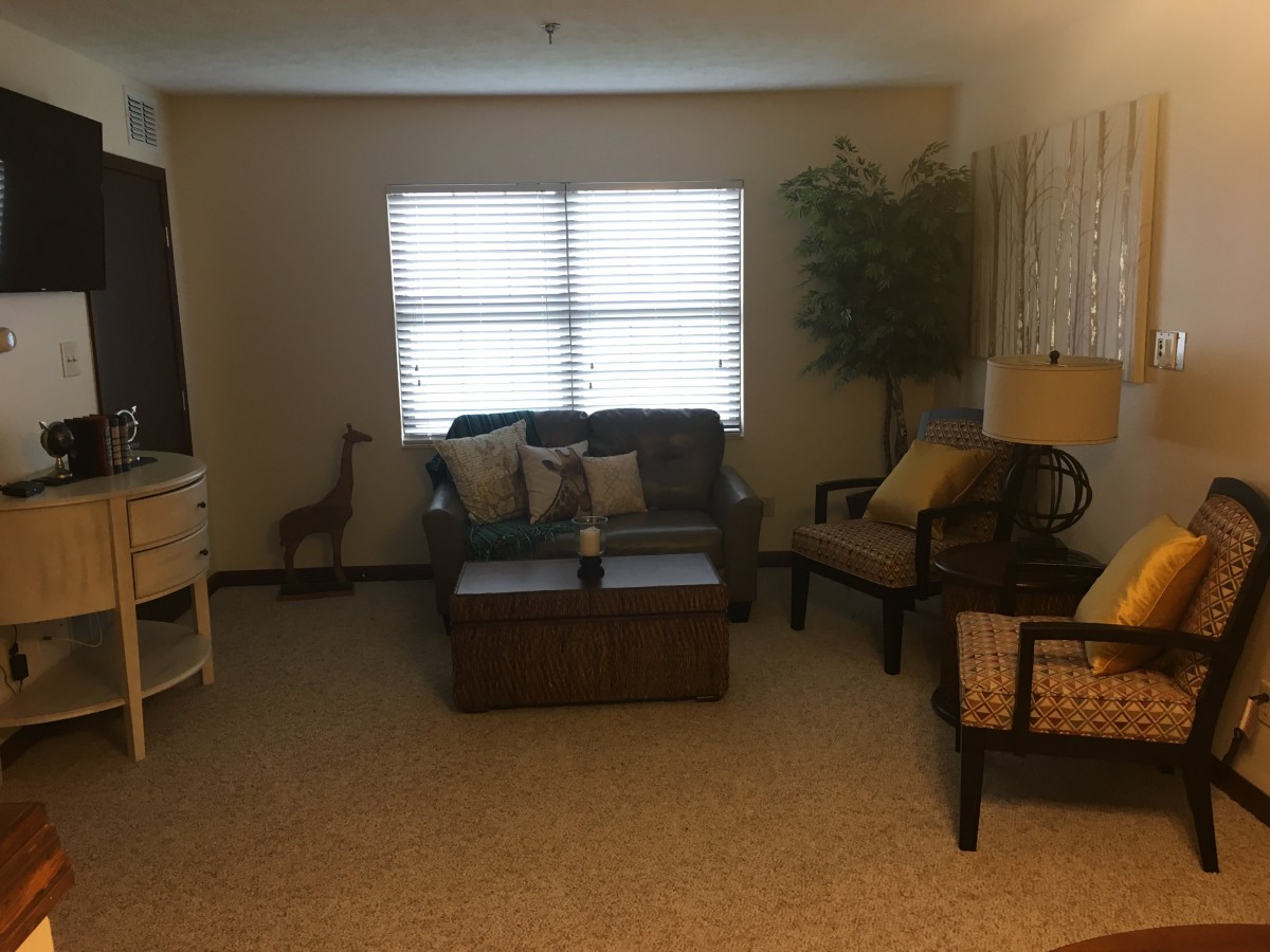 A cozy living room with sofas, armchairs, a coffee table, and a large window with curtains.